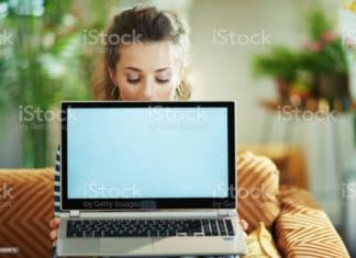 trendy woman and showing laptop blank screen trendy middle age housewife in blue blouse and striped jacket in the modern living room in sunny day sitting on couch and showing laptop blank screen. Adult Stock Photo
